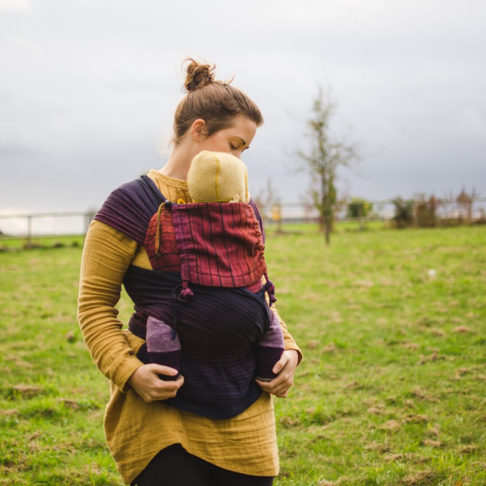 Mutter lächelt, Baby in der Trage WrapMysol Twilight schaut neugierig und streckt die Hand zum Fotografen